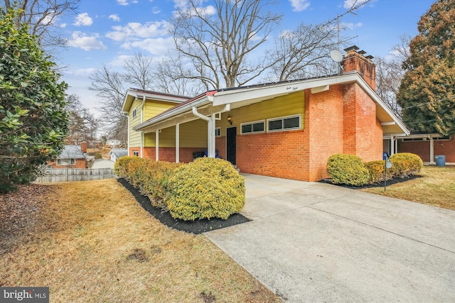 view of side of property featuring driveway, a yard, a chimney, and brick siding