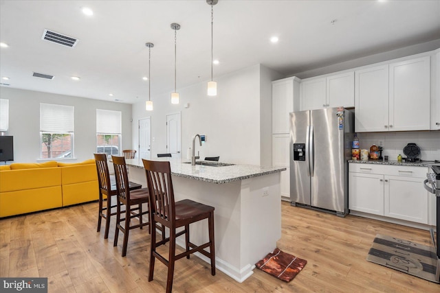 kitchen with white cabinetry, a center island with sink, stainless steel fridge, and light hardwood / wood-style floors