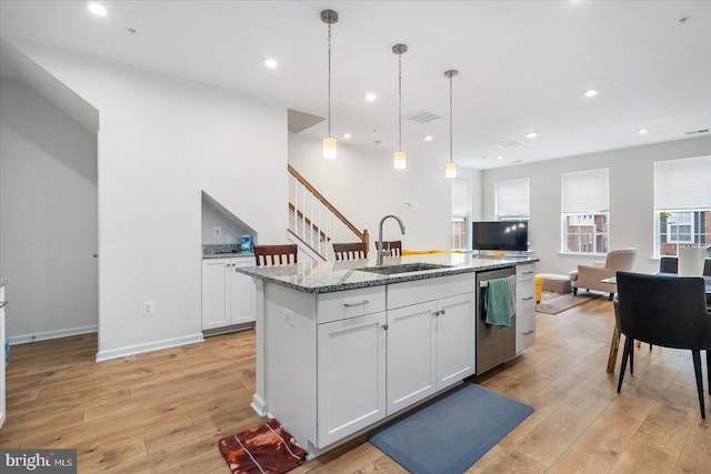 kitchen featuring light hardwood / wood-style floors, white cabinetry, stainless steel dishwasher, sink, and an island with sink