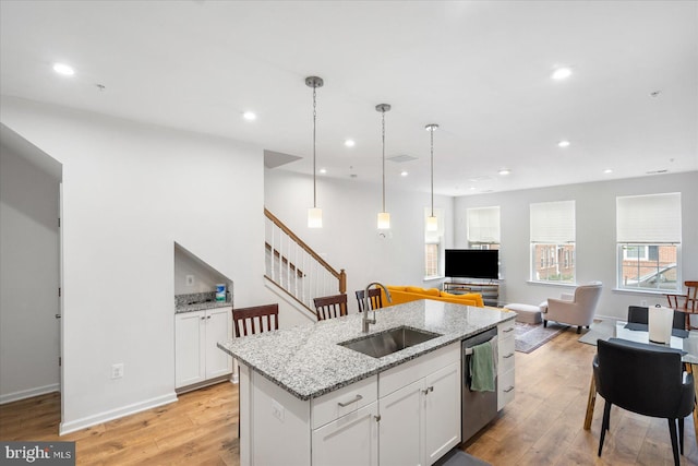 kitchen featuring light hardwood / wood-style flooring, dishwasher, sink, an island with sink, and light stone countertops