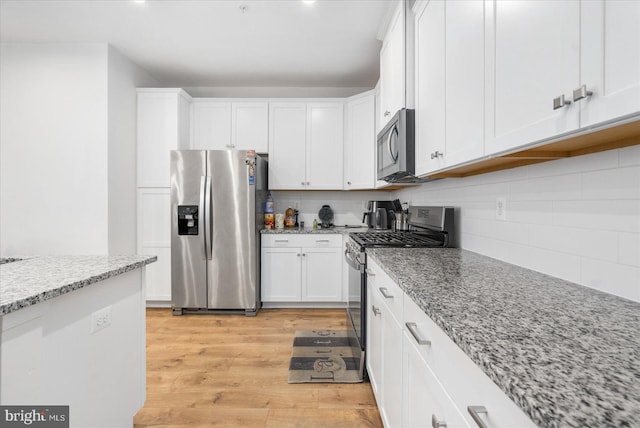 kitchen featuring light wood-type flooring, stainless steel appliances, decorative backsplash, and light stone countertops