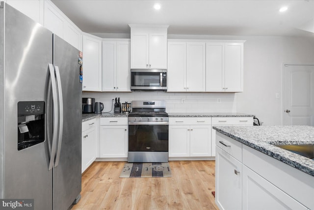 kitchen with appliances with stainless steel finishes, light hardwood / wood-style flooring, backsplash, white cabinetry, and light stone countertops