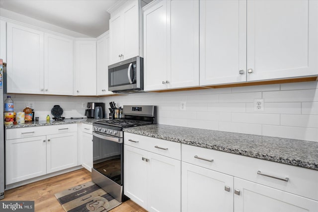 kitchen featuring appliances with stainless steel finishes, light hardwood / wood-style flooring, decorative backsplash, and white cabinetry