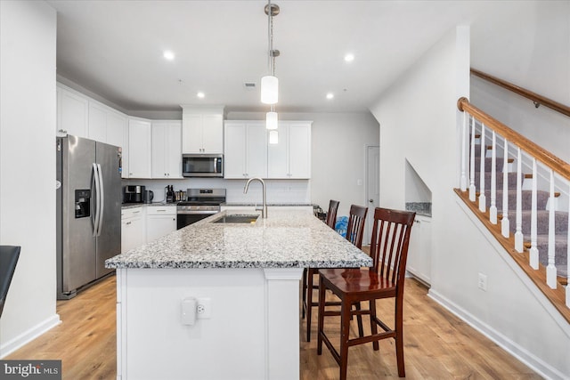 kitchen with sink, appliances with stainless steel finishes, light hardwood / wood-style flooring, light stone countertops, and an island with sink