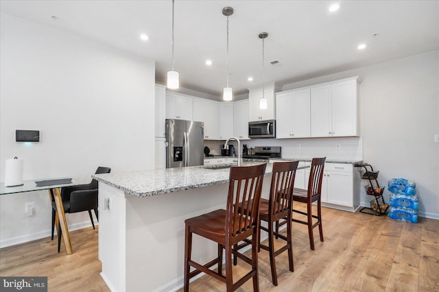 kitchen featuring a kitchen breakfast bar, light hardwood / wood-style flooring, an island with sink, appliances with stainless steel finishes, and light stone counters