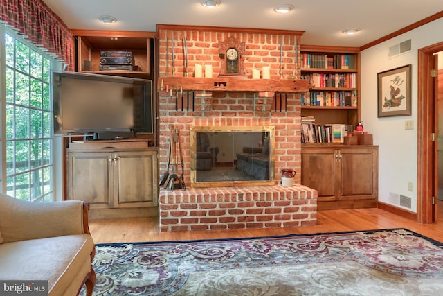 living area with a brick fireplace, crown molding, visible vents, and light wood-style floors