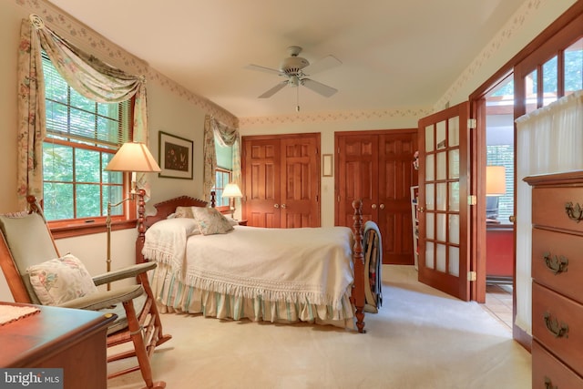 bedroom with ceiling fan, two closets, and light colored carpet