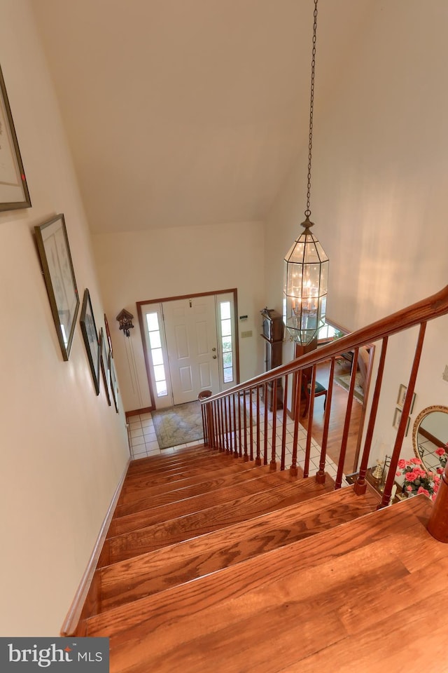 stairs featuring high vaulted ceiling, a notable chandelier, baseboards, and wood finished floors