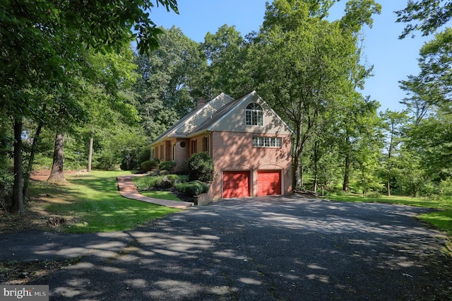 view of side of property with aphalt driveway, an attached garage, brick siding, a lawn, and a chimney