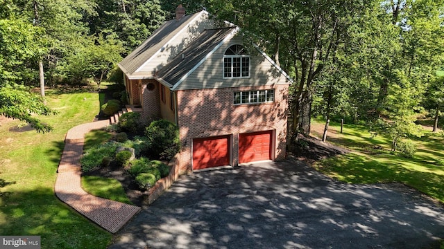 exterior space featuring brick siding, a yard, a chimney, an attached garage, and driveway