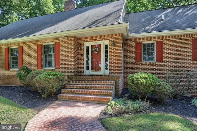 property entrance featuring a shingled roof, a chimney, and brick siding