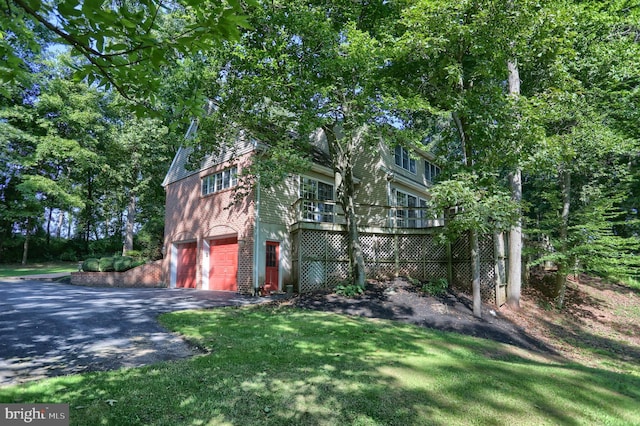 view of front facade with aphalt driveway, brick siding, a front yard, a garage, and a wooden deck