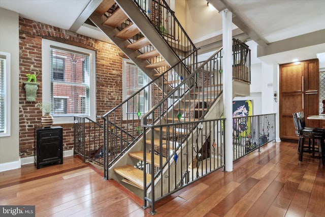 stairway with a towering ceiling, brick wall, baseboards, and wood finished floors