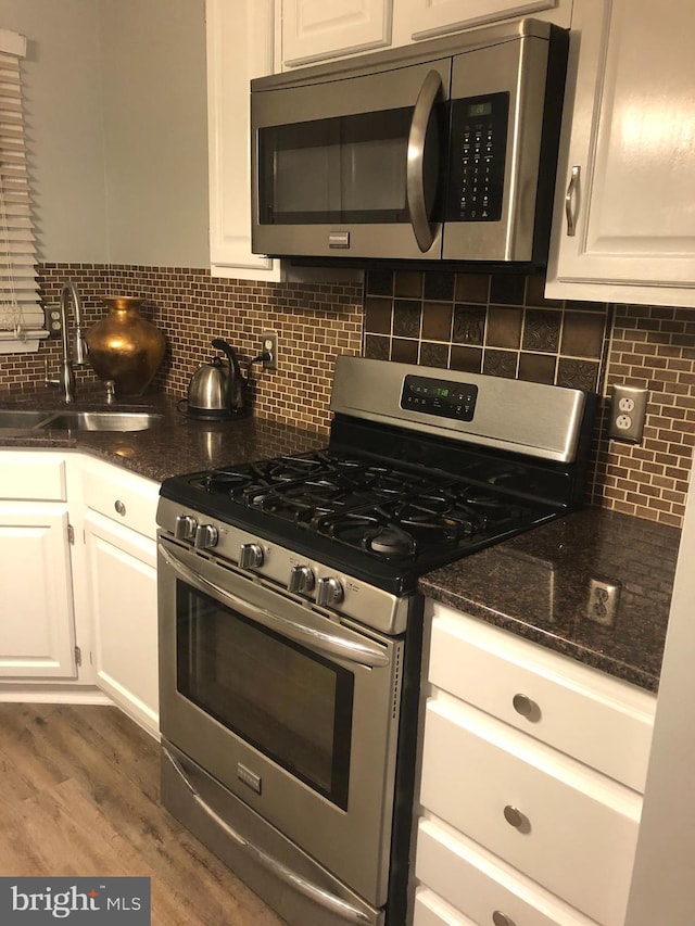 kitchen featuring white cabinets, backsplash, appliances with stainless steel finishes, wood-type flooring, and sink