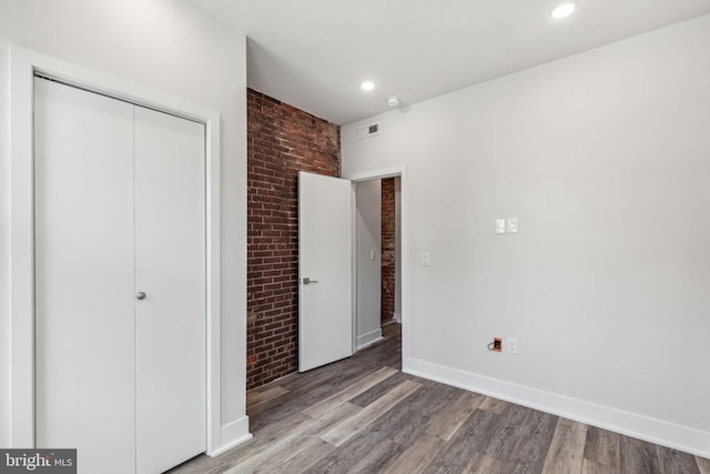 unfurnished bedroom featuring hardwood / wood-style flooring, brick wall, and a closet