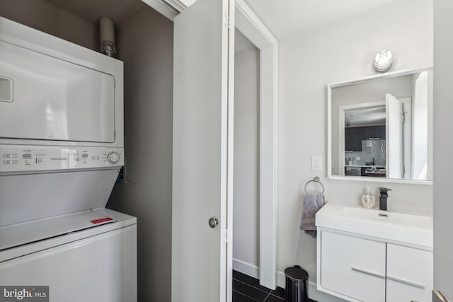 clothes washing area featuring stacked washer / dryer, sink, and dark tile patterned floors