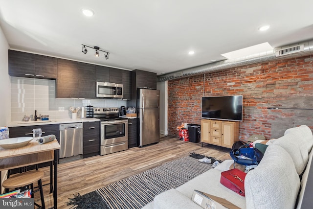 kitchen with sink, light wood-type flooring, appliances with stainless steel finishes, and decorative backsplash