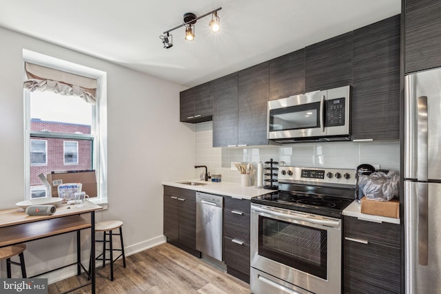 kitchen with appliances with stainless steel finishes, light hardwood / wood-style floors, sink, and tasteful backsplash