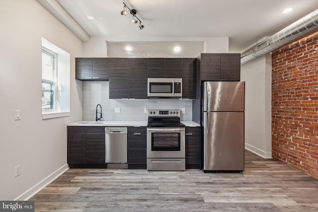 kitchen featuring sink, rail lighting, light hardwood / wood-style flooring, decorative backsplash, and stainless steel appliances