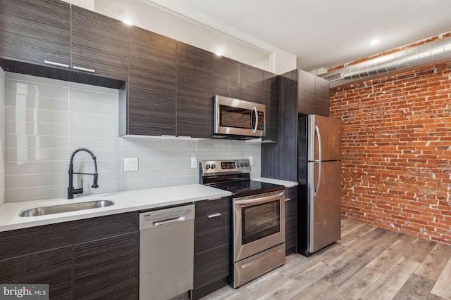 kitchen featuring appliances with stainless steel finishes, decorative backsplash, dark brown cabinets, sink, and light wood-type flooring