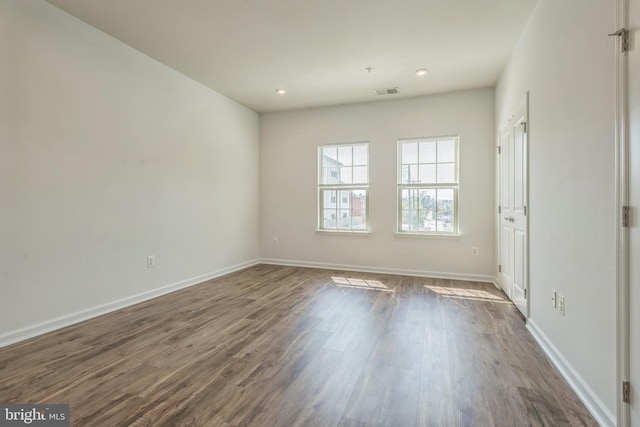 unfurnished room with dark wood-type flooring, visible vents, and baseboards