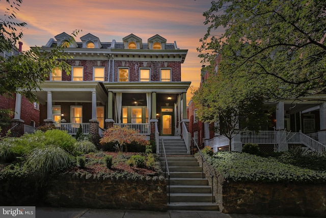 view of front of home with brick siding, a high end roof, a porch, stairs, and mansard roof