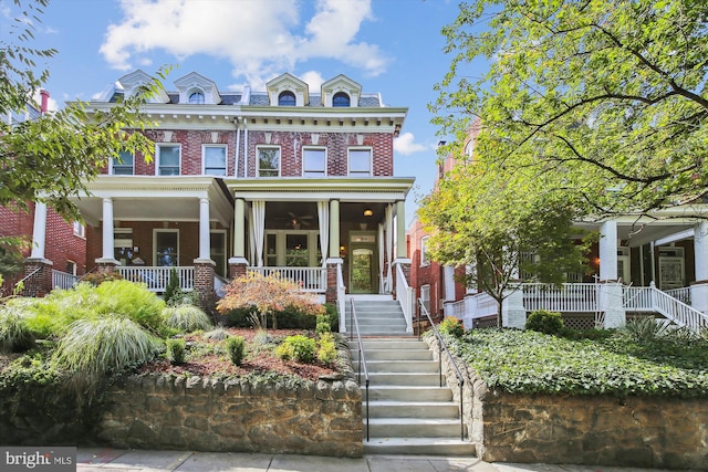 view of front of house featuring brick siding, a high end roof, a porch, stairs, and mansard roof