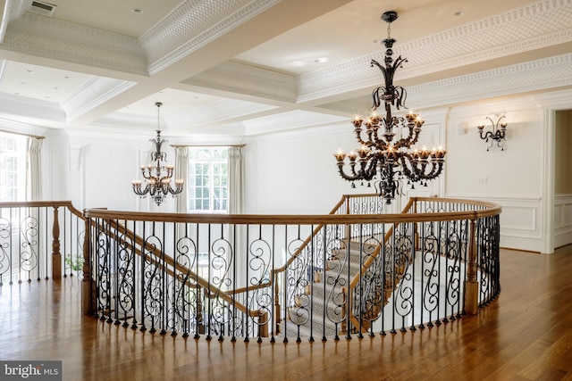 hall featuring a decorative wall, wood finished floors, an upstairs landing, beam ceiling, and an inviting chandelier