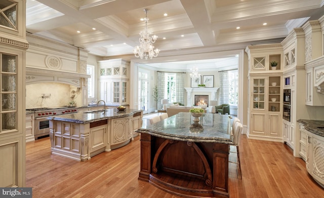 kitchen featuring a chandelier, a kitchen island with sink, a sink, cream cabinetry, and double oven range