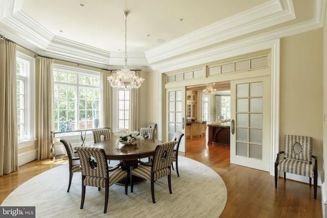 dining area with wood finished floors, ornamental molding, french doors, a tray ceiling, and an inviting chandelier