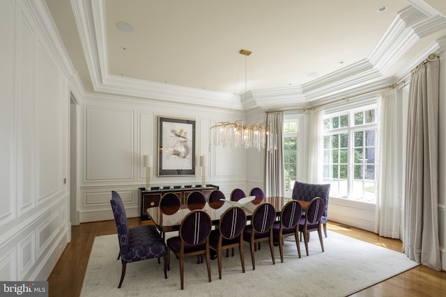 dining room featuring a notable chandelier, crown molding, a decorative wall, and wood finished floors