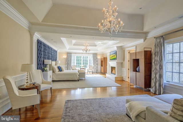 bedroom featuring a tray ceiling, a wainscoted wall, an inviting chandelier, wood finished floors, and a warm lit fireplace