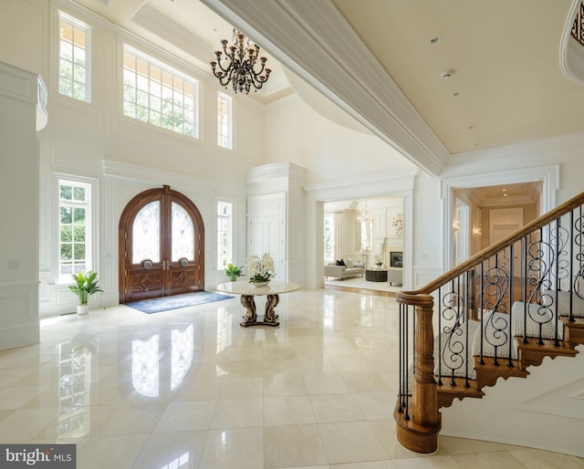 entrance foyer with a chandelier, a decorative wall, stairs, french doors, and crown molding