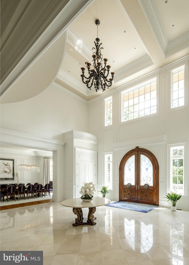 foyer featuring a high ceiling, ornamental molding, a chandelier, and french doors