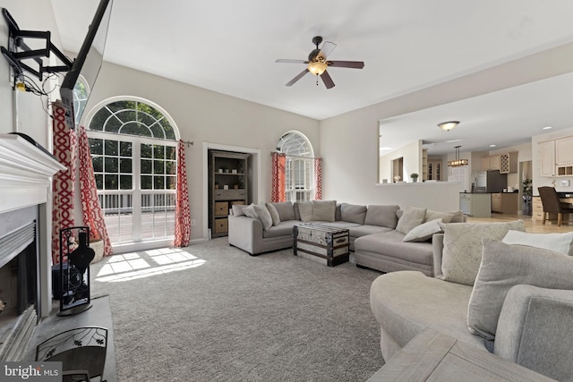 living area featuring a fireplace, a ceiling fan, and light colored carpet