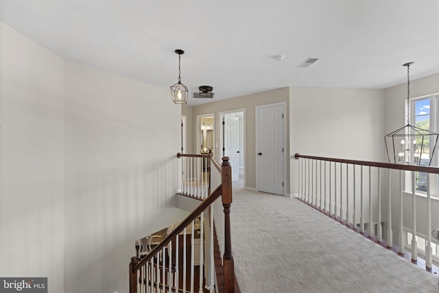 hallway with baseboards, visible vents, an inviting chandelier, an upstairs landing, and carpet floors