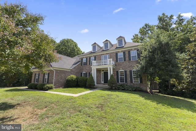 colonial-style house featuring a balcony, a front lawn, and brick siding