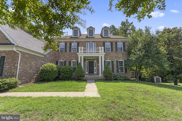 colonial-style house featuring brick siding, a balcony, and a front lawn