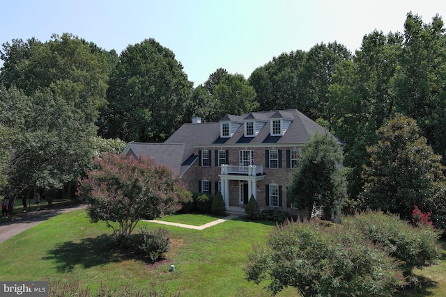 colonial inspired home featuring brick siding, a front lawn, and a balcony