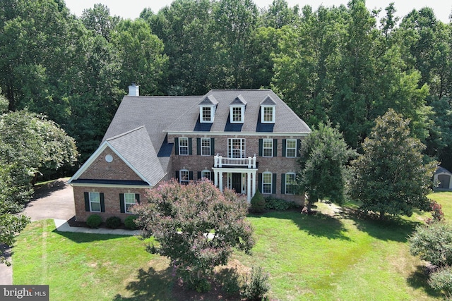 georgian-style home with brick siding, a front yard, a balcony, and a view of trees