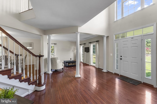 entrance foyer featuring a healthy amount of sunlight, dark wood-style floors, and decorative columns