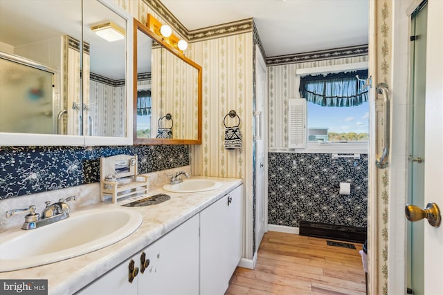 bathroom featuring double vanity, wallpapered walls, a sink, and wood finished floors