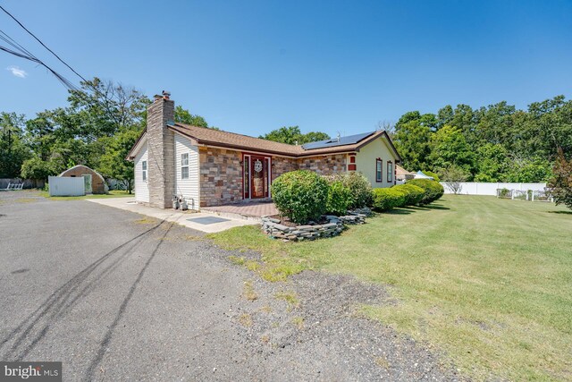 single story home with a front yard, solar panels, an outdoor structure, and a garage