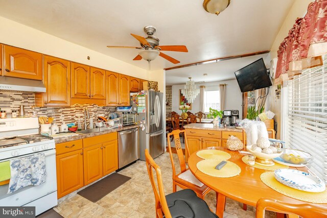 kitchen with light tile patterned flooring, ceiling fan with notable chandelier, stainless steel appliances, and tasteful backsplash