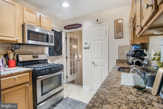 kitchen with light tile patterned floors, backsplash, dark stone countertops, stainless steel appliances, and a sink