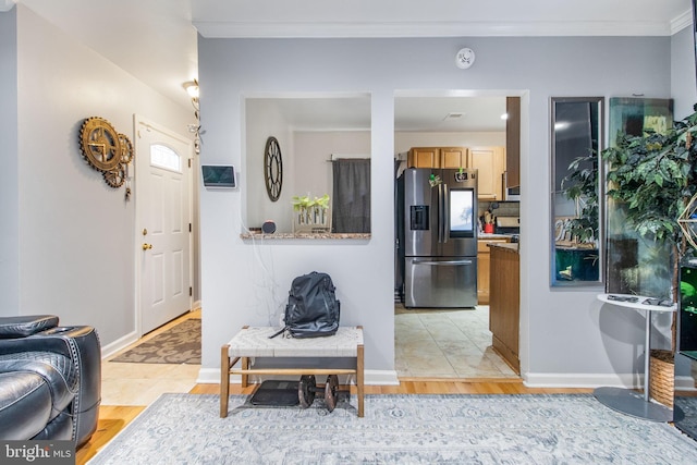 kitchen with light wood-type flooring, ornamental molding, light countertops, and stainless steel fridge with ice dispenser