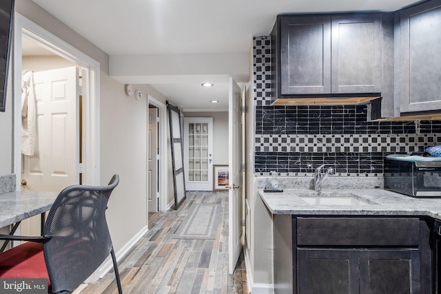 kitchen featuring light stone counters, sink, light hardwood / wood-style floors, a barn door, and backsplash