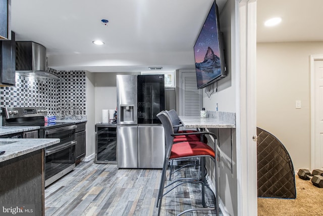 kitchen with beverage cooler, wall chimney exhaust hood, backsplash, light hardwood / wood-style flooring, and appliances with stainless steel finishes