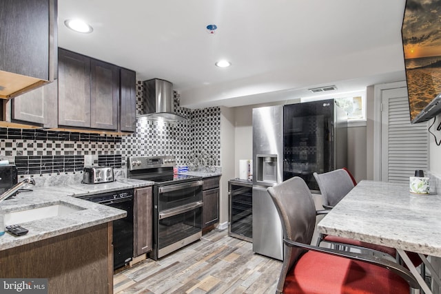 kitchen with beverage cooler, wall chimney exhaust hood, appliances with stainless steel finishes, and dark brown cabinetry