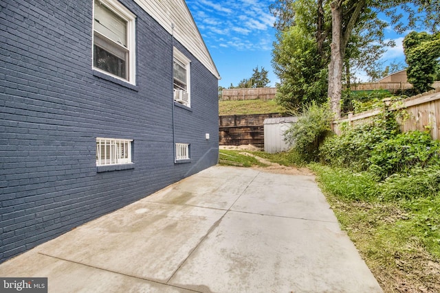 view of side of property with a patio area, fence, and brick siding